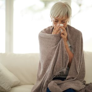 woman blowing her nose at home sick