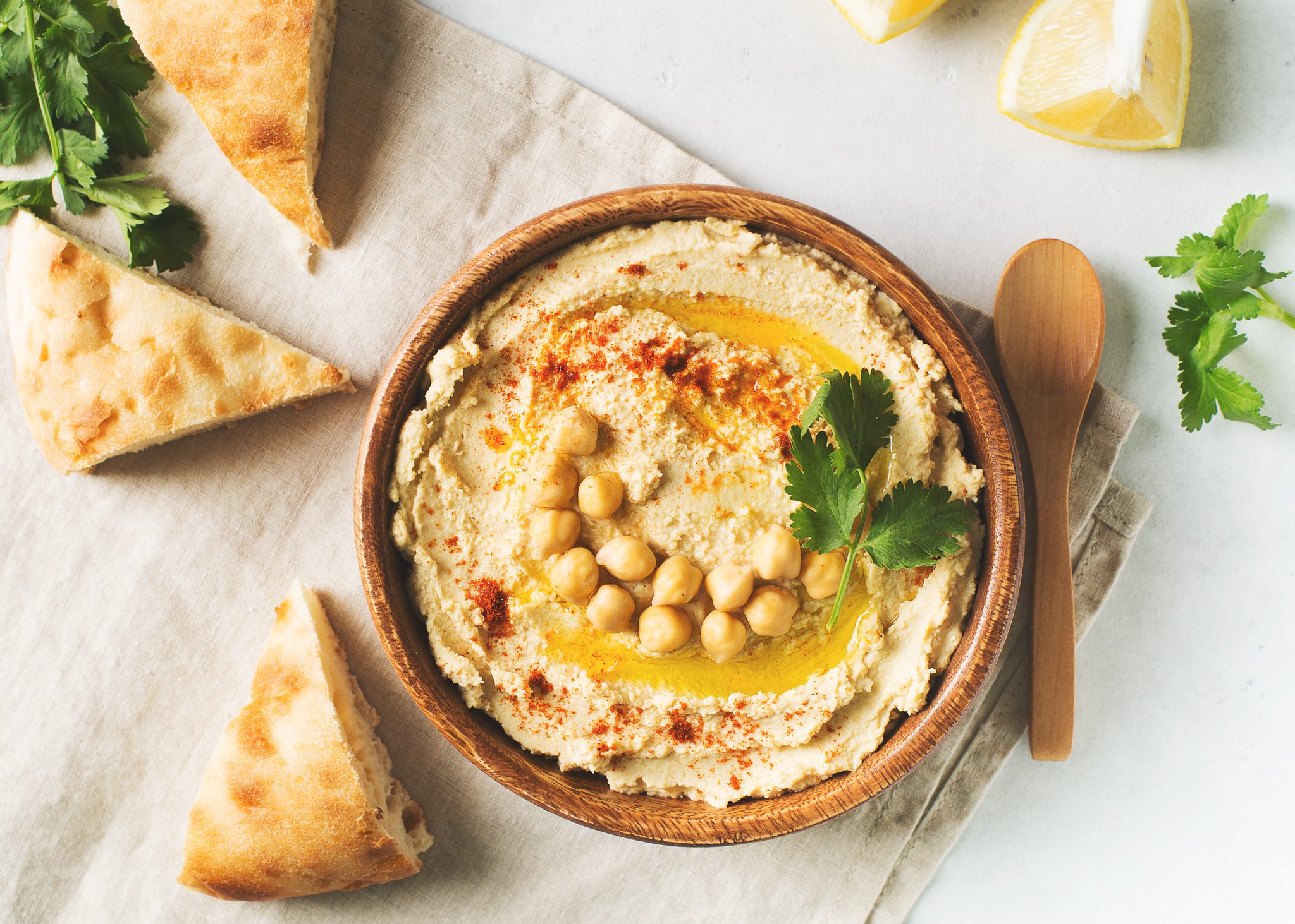 Hummus dip with chickpea, pita and parsley in wooden plate on white background