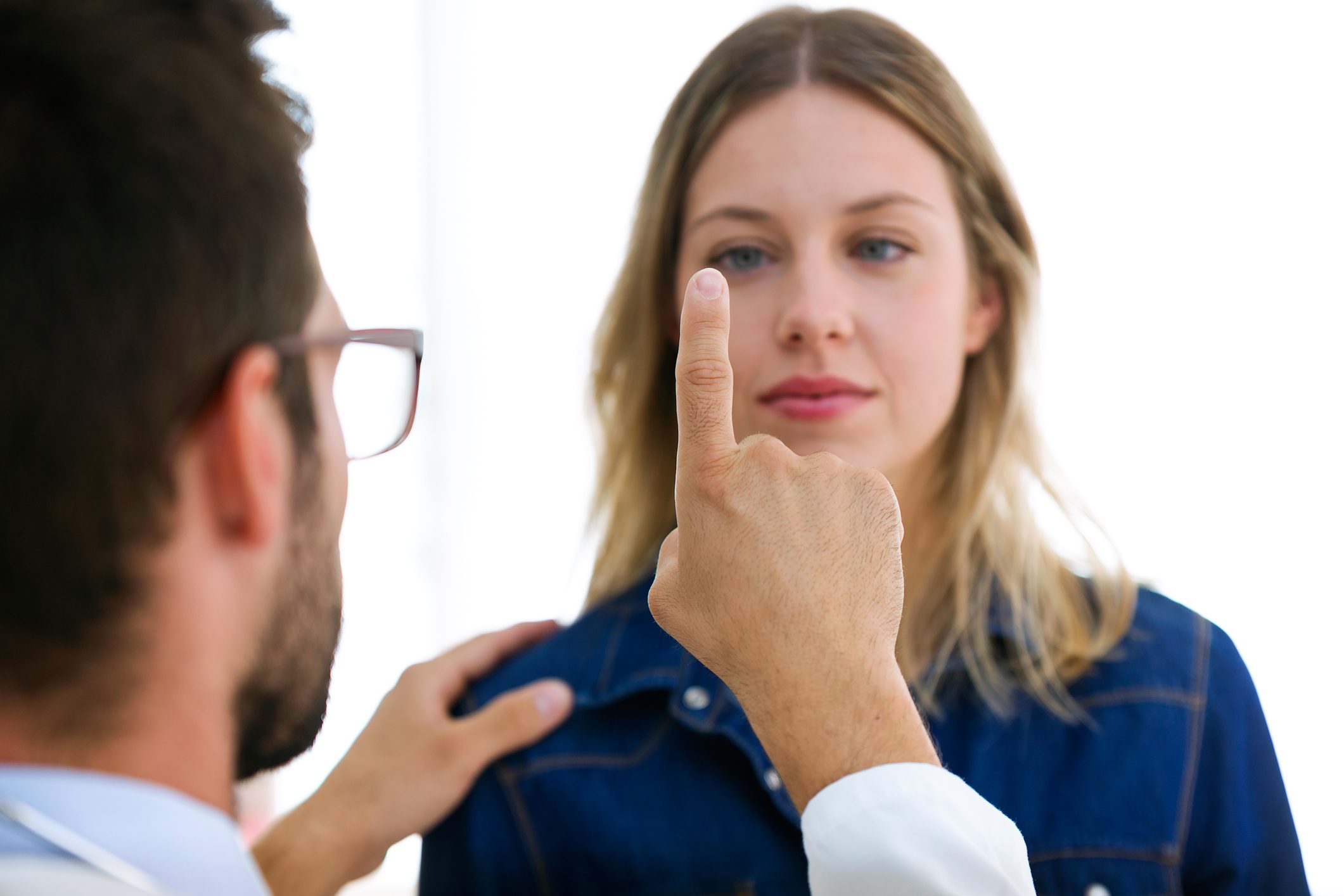 Attractive male doctor ophthalmologist checking the eye vision of beautiful young woman in modern clinic.
