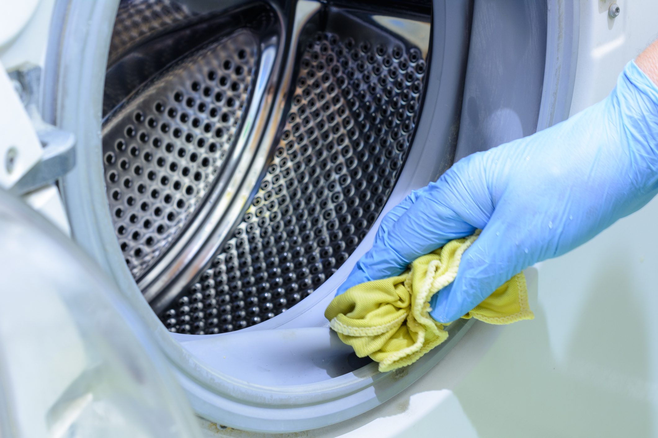 Cleaning the bathroom. Woman is cleaning washer (washing machine) with a rag in rubber gloves.