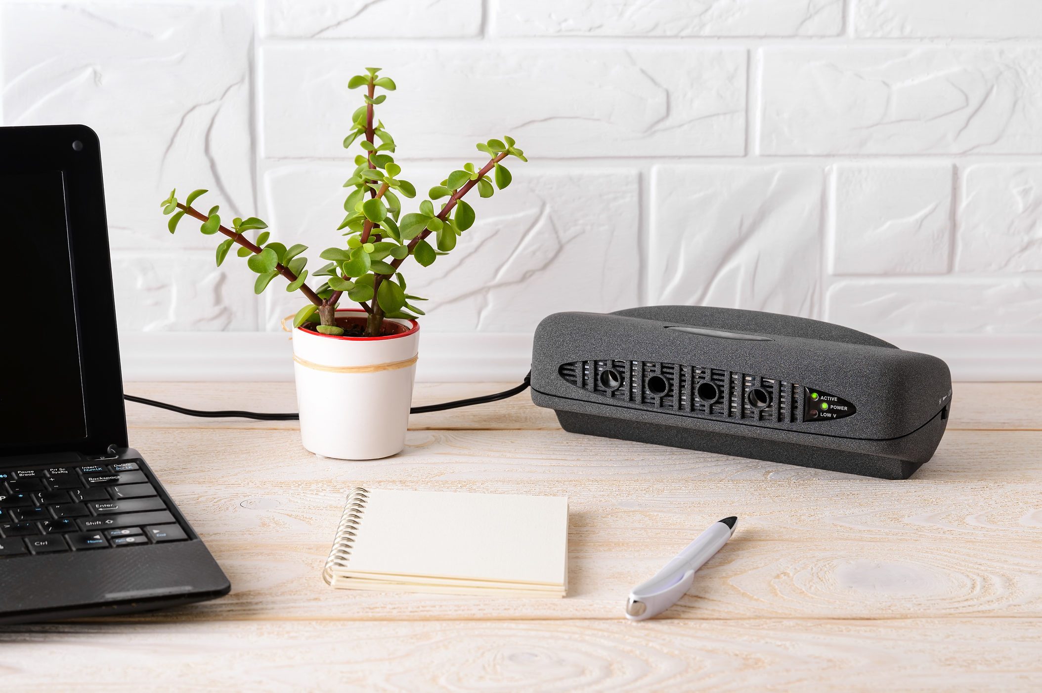 Black air ionizer near laptop on a white wooden table