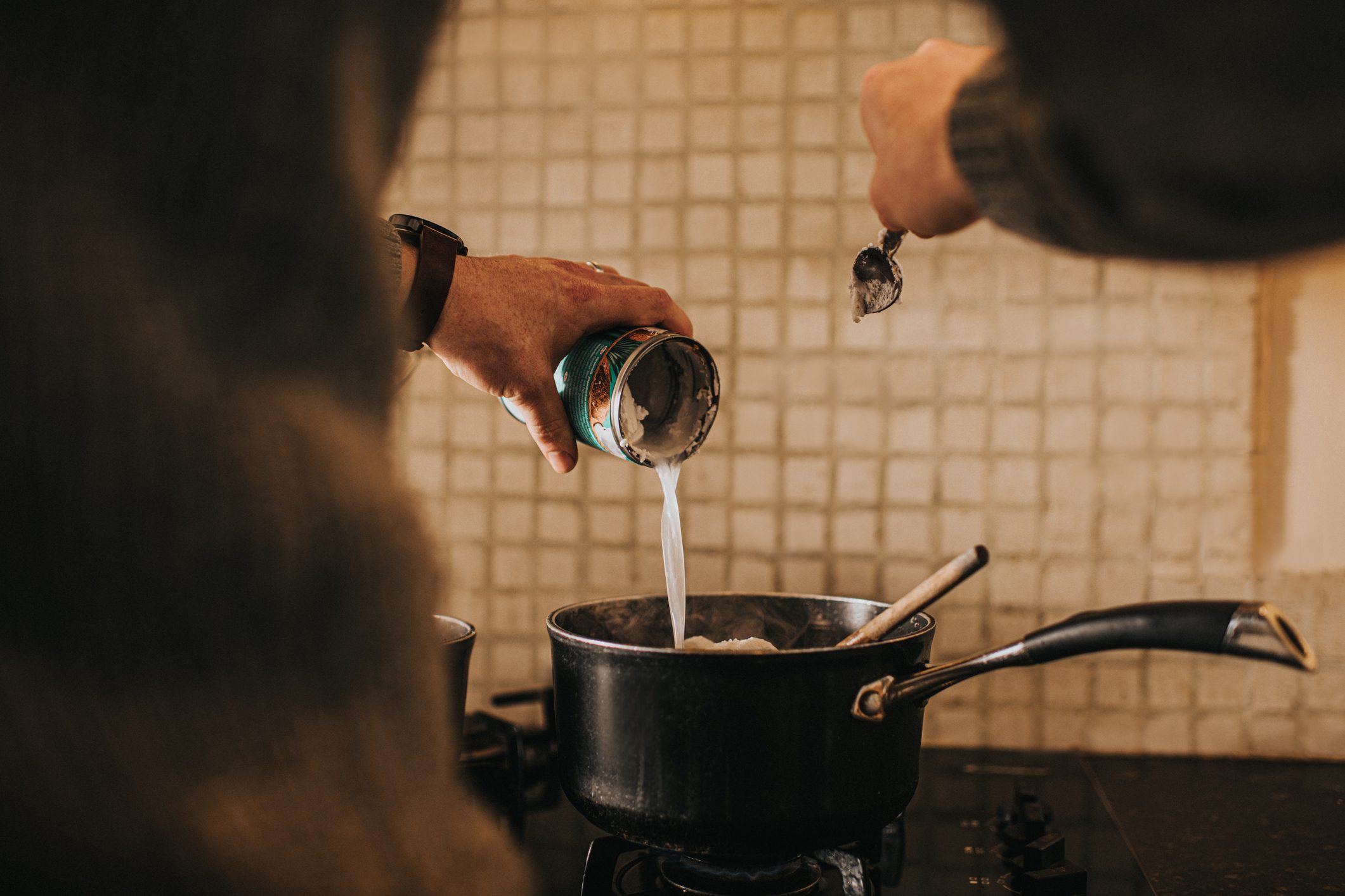 pouring coconut milk into saucepan over the stove