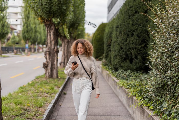 Young woman using smart phone while walking on footpath in city