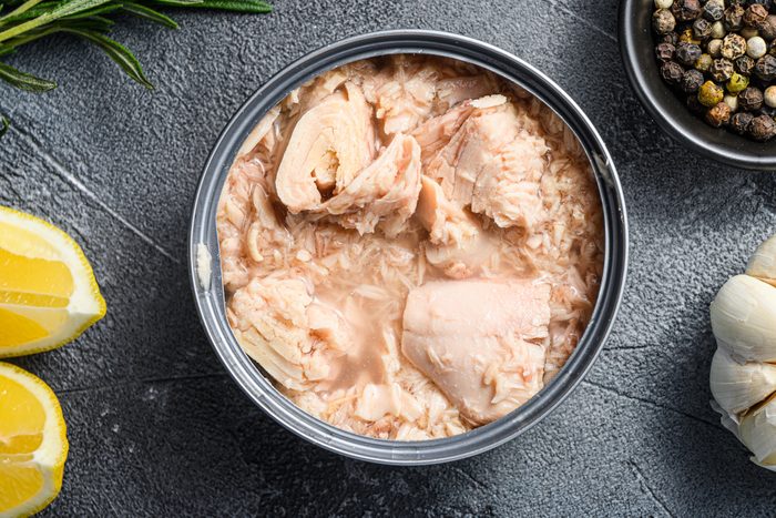 canned tuna open can with fresh herbs garlic and lemon ingredients for preservs top view close up