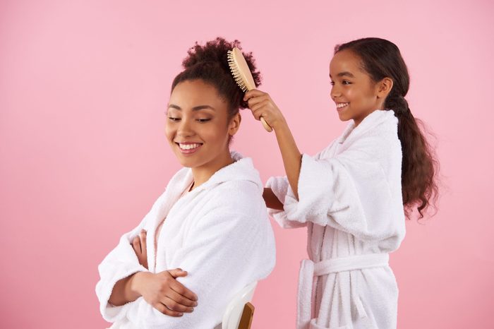 Little African American girl is combing mother hair. Isolated on pink background. Studio portrait.