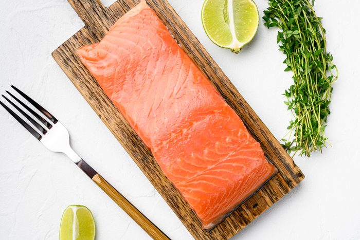 Portioned raw salmon fillet, with herbs, on white stone table background, top view flat lay