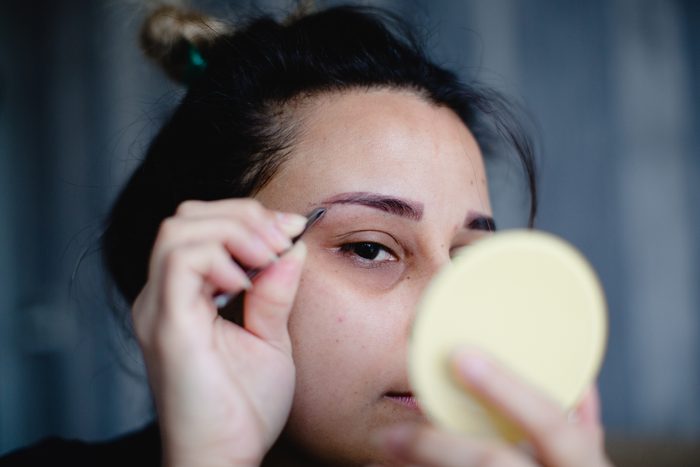 A woman looking at mirror and plucking her eyebrows