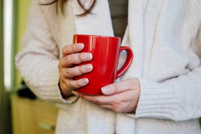 Woman holding red cup of hot drink at home.