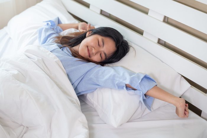 Young Asian woman stretching in bed after wake up in the morning