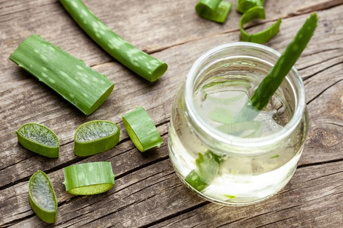 Aloe Vera gel cream for skin and body care. Aloe pulp slices in a glass jar and leaves on a wooden table. Cosmetic lotion