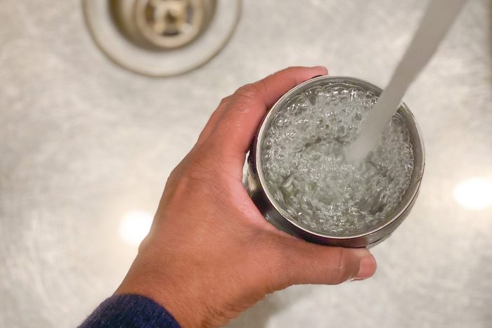 unrecognizable african-american woman fills a reusable cup with tap water
