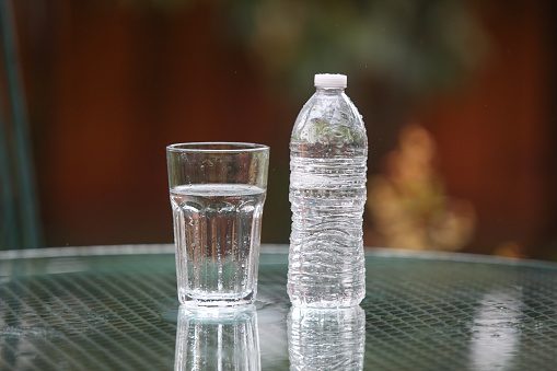 Glass of drinking water and a plastic water bottle sitting outdoors on a table