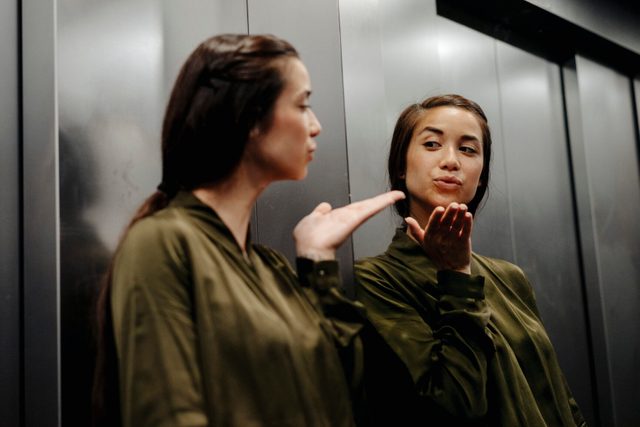 Young woman looking in mirror in elevator blowing a kiss